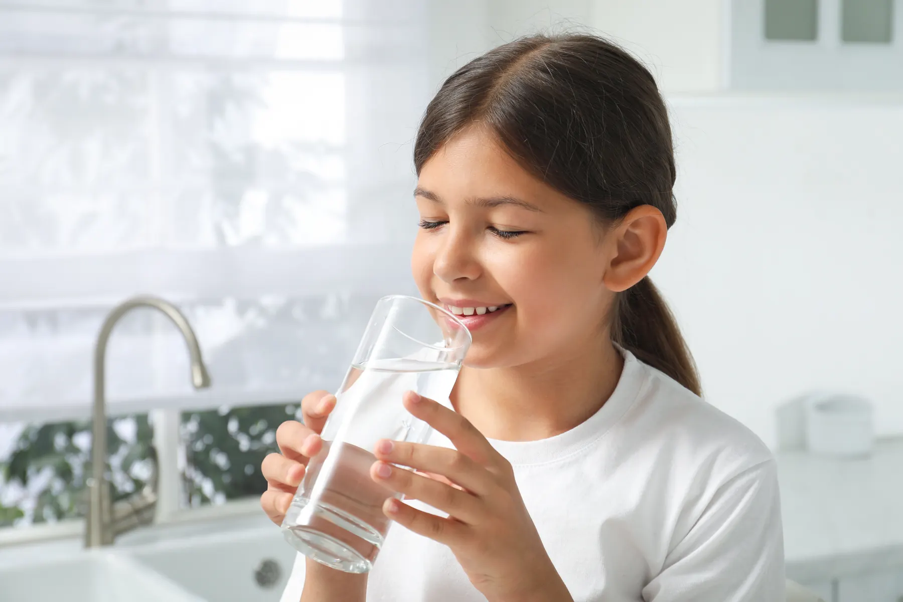 A girl having a drink of water in a bright kitchen